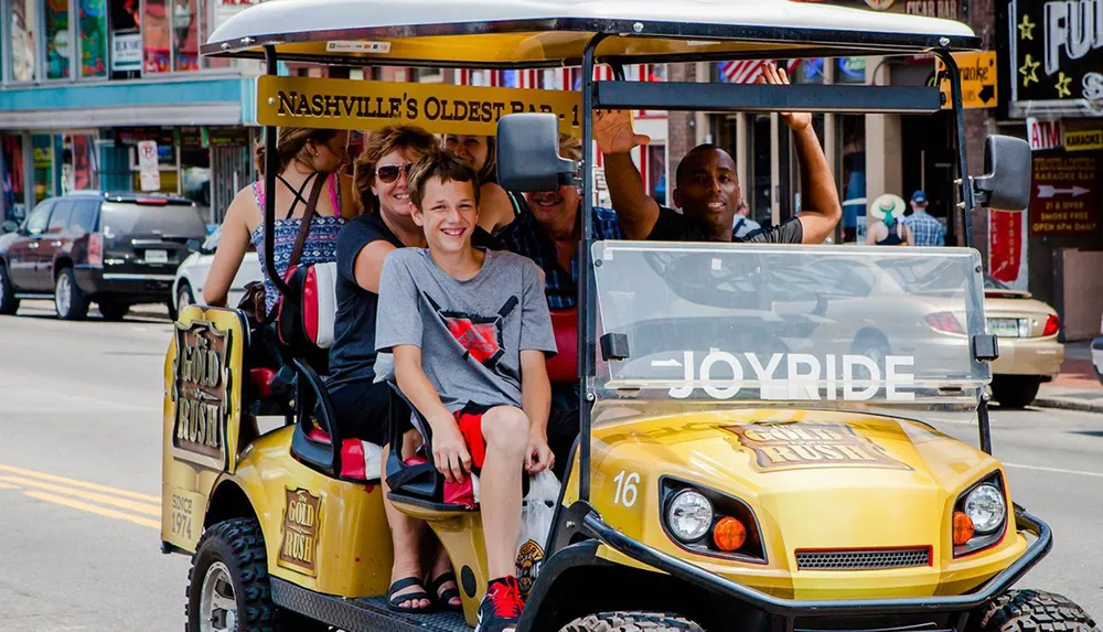 A group of people is enjoying a tour on a unique golf cart-like vehicle labeled JOYRIDE on a vibrant city street