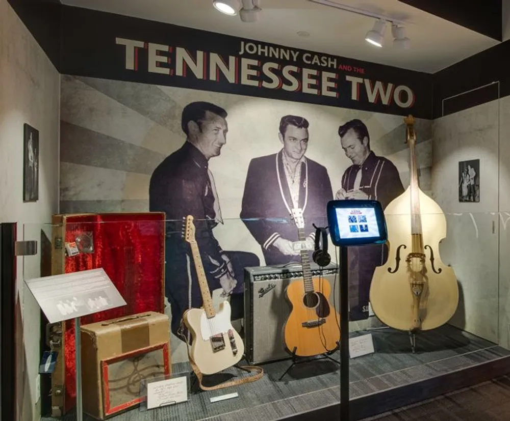 The image is of a museum exhibit dedicated to Johnny Cash and the Tennessee Two featuring musical instruments memorabilia and images related to the artists