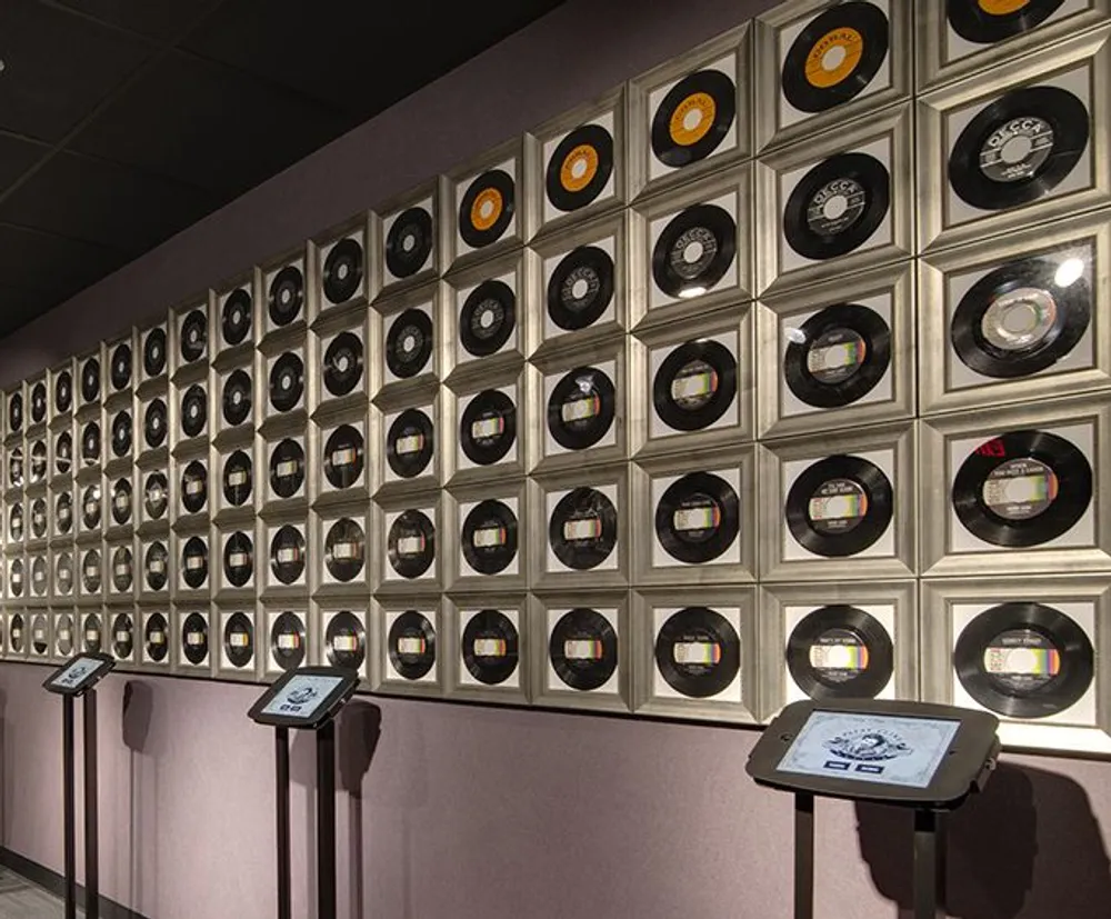 The image shows a wall display of gold and platinum record awards possibly in a museum or exhibition representing musical achievements