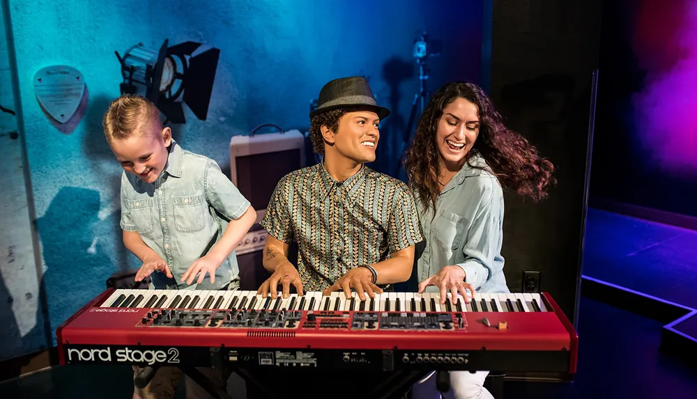 A child and a woman smile as they pose with a wax figure of a man at a keyboard in an exhibit