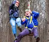 A smiling person is equipped with a harness and safety gear on a high ropes course among trees