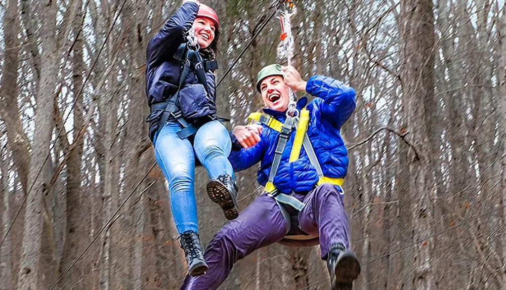 Two people are joyfully zip-lining through a wooded area