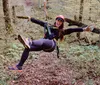 A smiling person is equipped with a harness and safety gear on a high ropes course among trees