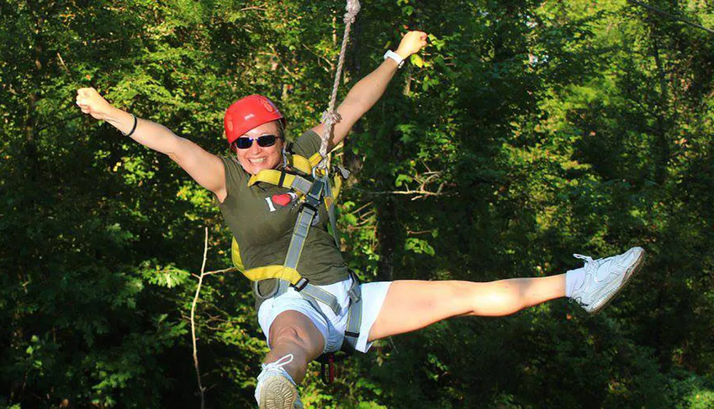 A person is gleefully experiencing a zipline adventure among the trees wearing a helmet and a harness for safety