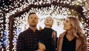 A family of three is sharing a moment of wonder under a canopy of twinkling lights.