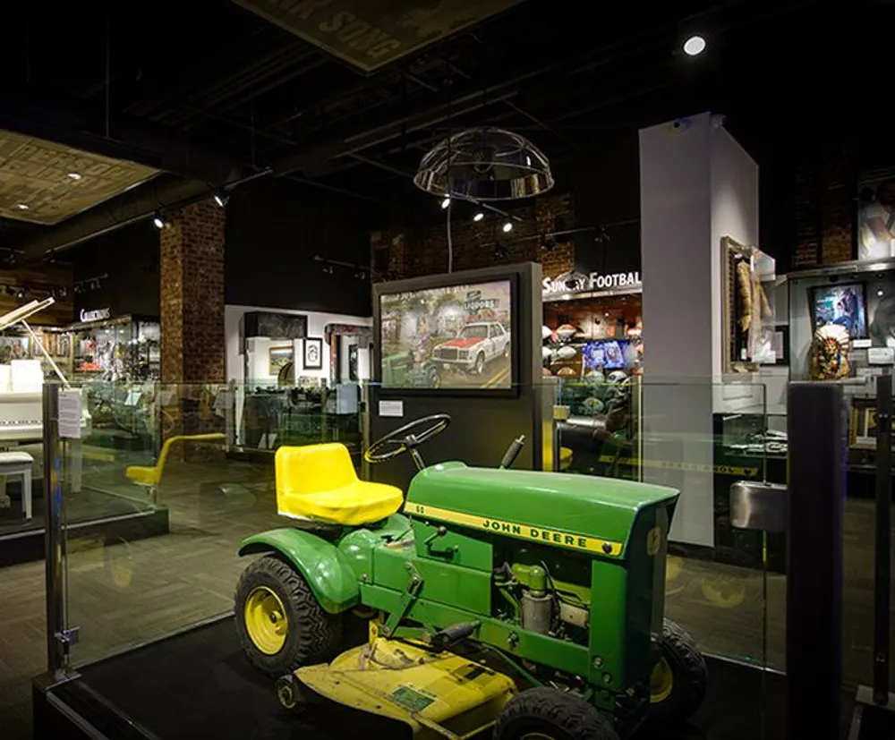 The image shows an interior space with a vintage John Deere tractor on display likely in a museum or exhibit with various memorabilia and artwork on the walls