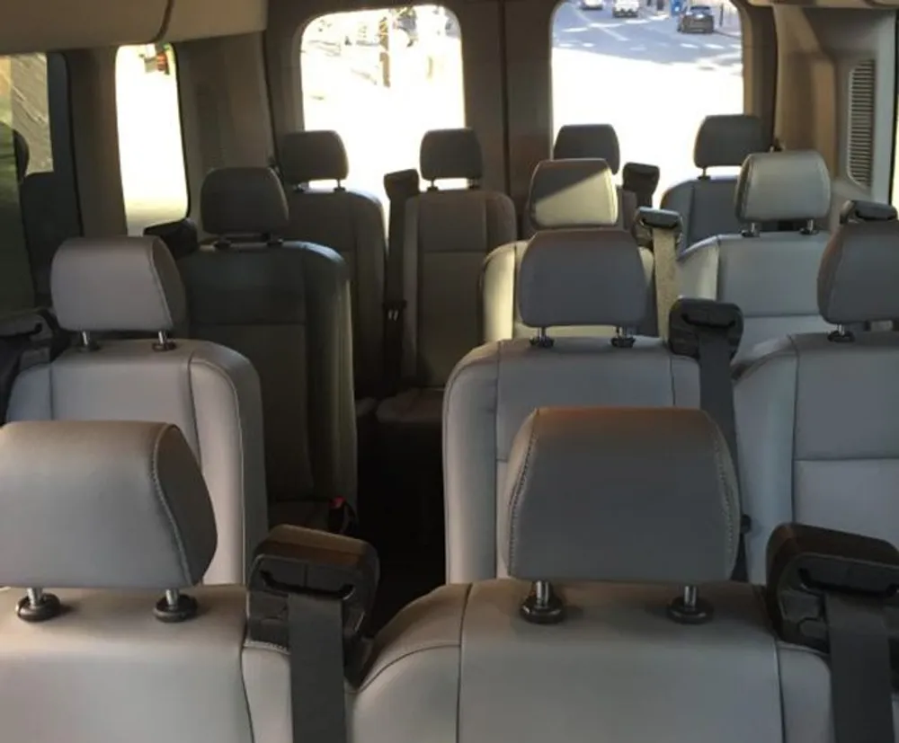 The image shows the interior of a spacious vehicle with several rows of empty grey seats likely a van or a large SUV taken from the rear looking toward the front windows