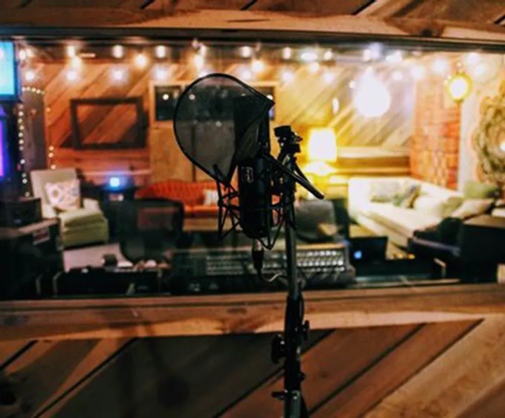 The image shows a recording studio with a microphone in the foreground and musical equipment and cozy furnishings in the background