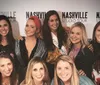Five people are posing for a photo with smiles at a Nashville Studio Tour event where one person is holding a guitar