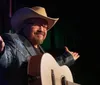 A musician in a cowboy hat is performing with an acoustic guitar on a stage singing into a microphone