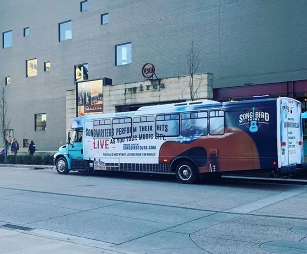A colorful bus with an advertisement for live songwriter performances is parked on a city street