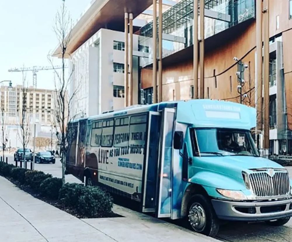 A turquoise and white bus with text on its side is parked on a city street with modern buildings in the background