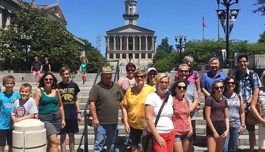 A diverse group of people are posing for a photo in front of a large building with a central dome on a sunny day.