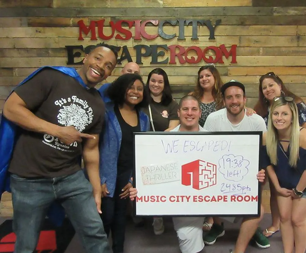 A group of smiling people is posing with a sign that says We Escaped indicating their success at a Japanese Thriller escape room challenge at Music City Escape Room