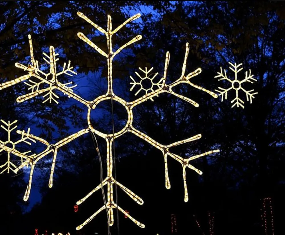 The image shows an illuminated snowflake-shaped decoration against a dusky or evening sky with a silhouette of trees in the background