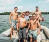 A group of cheerful men in swimwear are having a good time on a boat some holding beverages on a sunny day