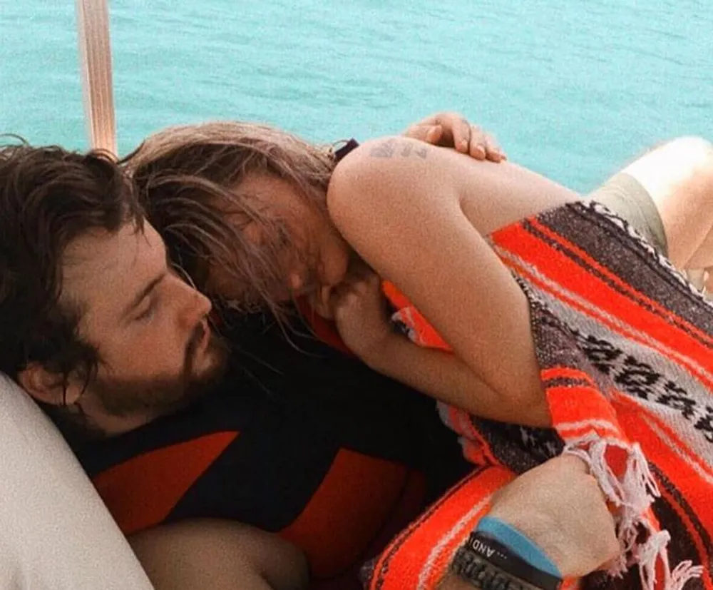 Two people are affectionately embracing each other while relaxing on a boat with clear turquoise water in the background
