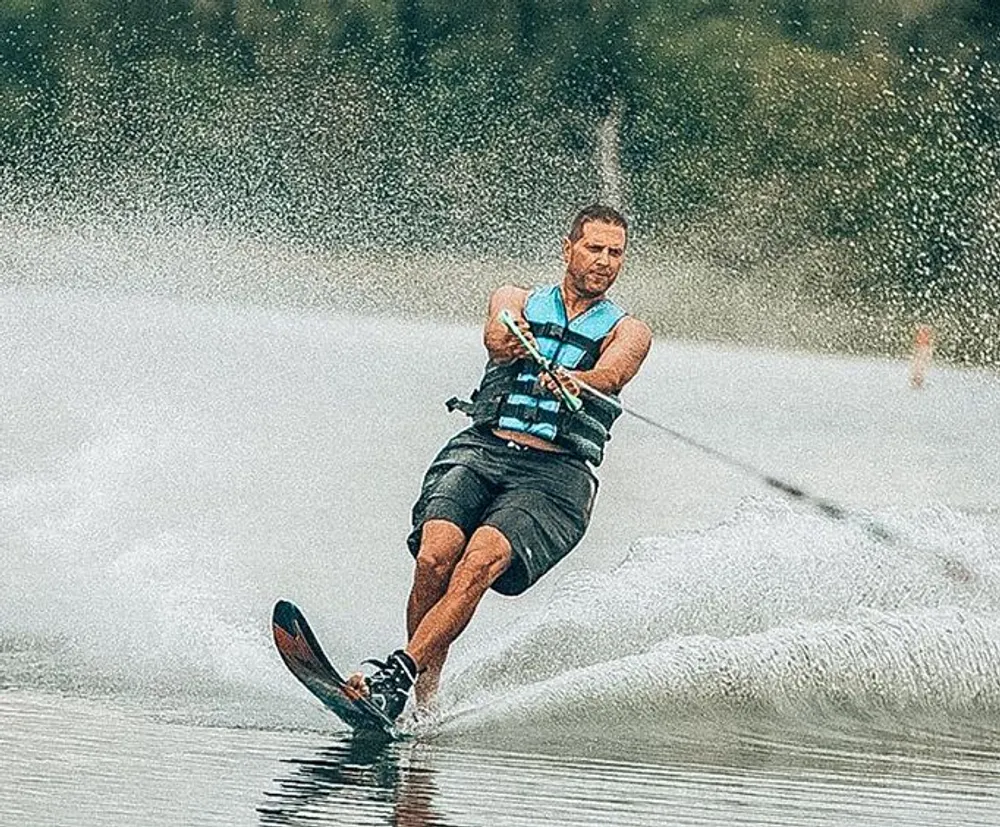 A focused individual is waterskiing creating a dynamic spray of water as they carve through a lake