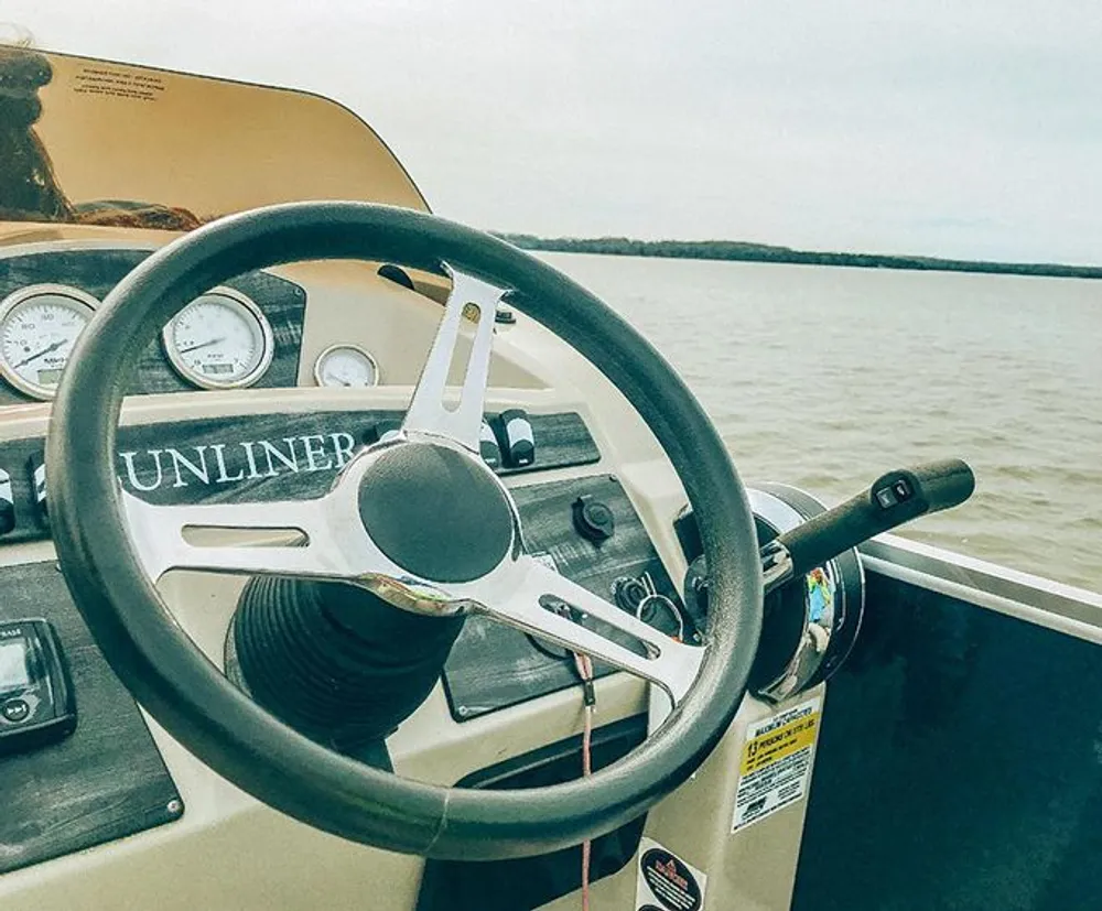 The image shows a boats steering wheel and control panel with a view of the water in the background