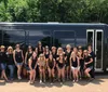 A group of people is posing for a photo in front of a black bus on a sunny day