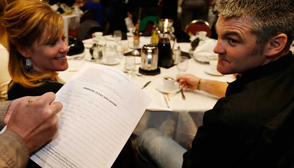 A smiling woman is showing a man a document at a table with coffee cups and dinnerware indicating a social or professional event setting