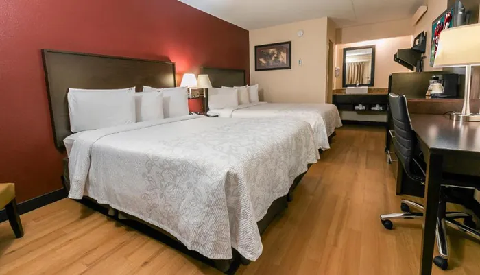 The image shows a neatly arranged hotel room with two beds a work desk and red accent walls