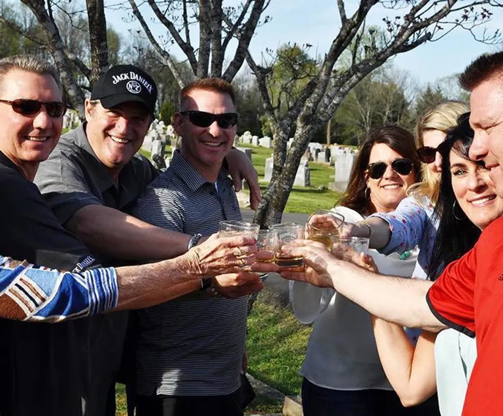 A group of people are smiling and toasting with drinks in a cemetery