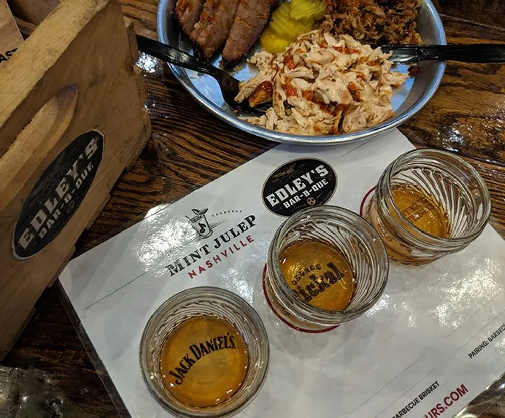 The image shows a table at a barbecue restaurant with a plate of food three glasses of whiskey and a menu featuring the Mint Julep and Edleys Bar-B-Que branding