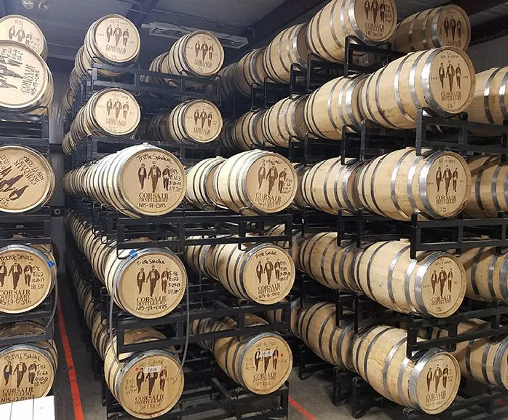 Rows of wooden barrels are stacked on metal racks in a storage room presumably for aging spirits such as whiskey or wine