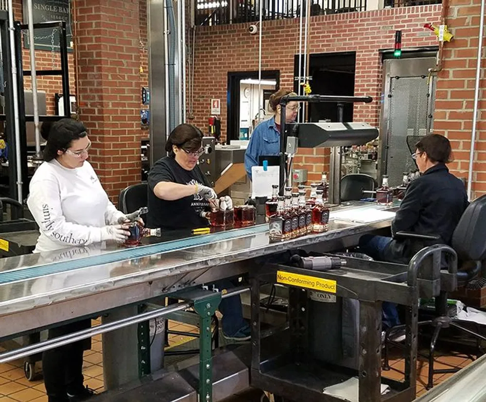 Workers are inspecting and manually handling bottles on a production line inside a distillery or bottling plant