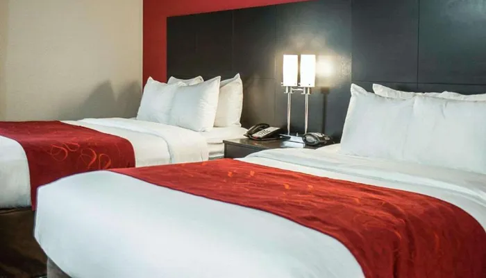 A hotel room with two neatly made beds featuring white linens and red decorative runners beside a nightstand with a lamp and a phone