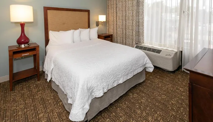 The image shows a neatly arranged hotel room with a large bed nightstands lamps and a window with curtains