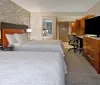 The image shows a modern hotel room with twin beds an office chair and desk and a flat-screen TV