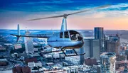 A helicopter is flying over a cityscape during twilight, with buildings illuminated against a dusky sky.