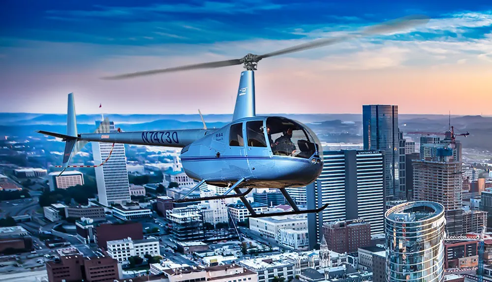 A helicopter is flying over a cityscape during twilight with buildings illuminated against a dusky sky