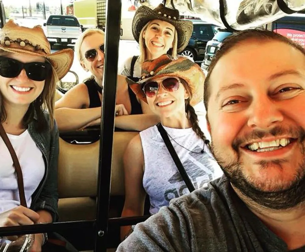 A group of happy people some wearing cowboy hats are taking a selfie together inside a vehicle