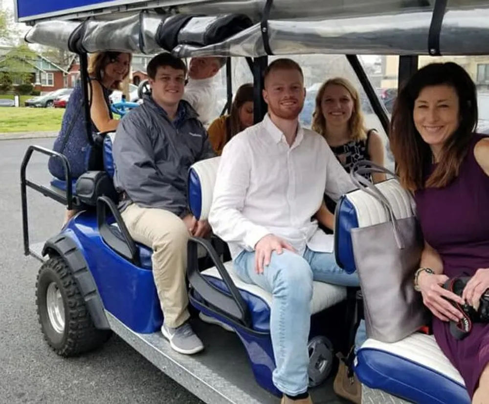 A group of people are smiling as they sit in a blue and white golf cart-like vehicle