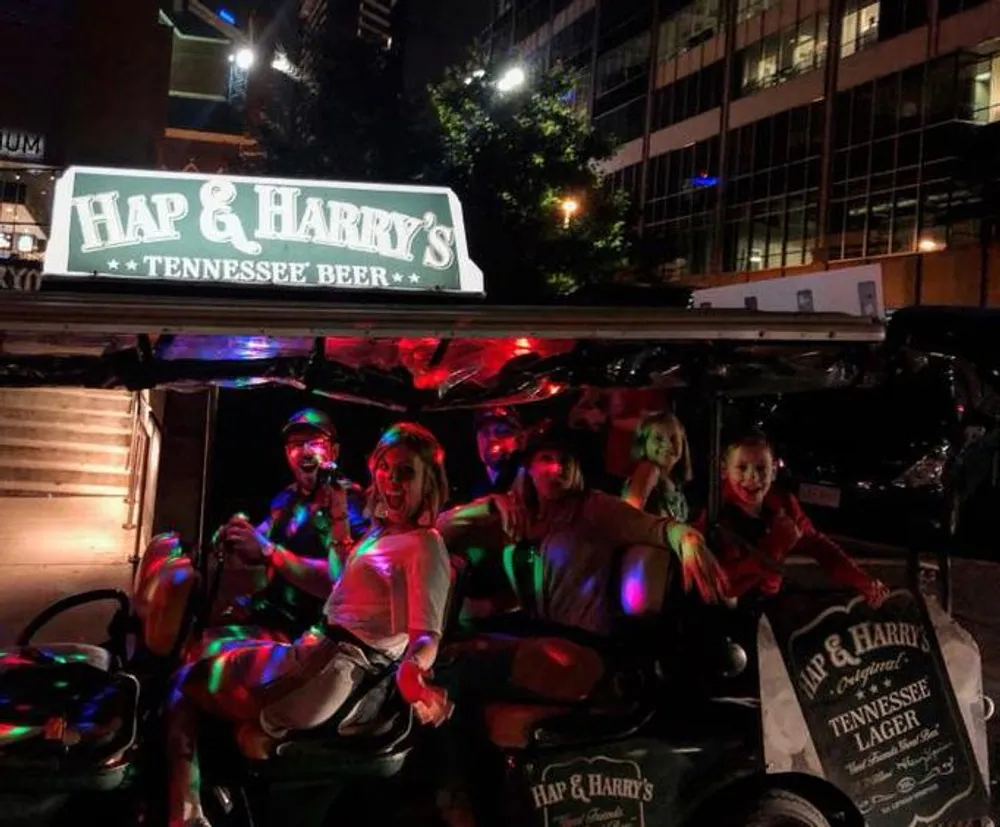 A group of people is having fun on a night out riding a party bike adorned with lights under a sign for Hap  Harrys Tennessee Beer
