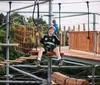 A person is navigating a rope course while wearing safety gear on a sunny day