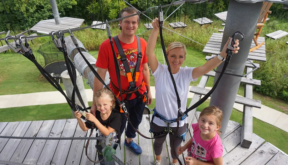 A happy family of four equipped with safety harnesses is posing for a photo before embarking on a high ropes adventure course