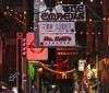 A group of people is gathered on a lively urban night street with neon signs and a sign for Korean Vets Bridge in the background