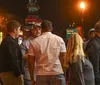 A group of people is gathered on a lively urban night street with neon signs and a sign for Korean Vets Bridge in the background