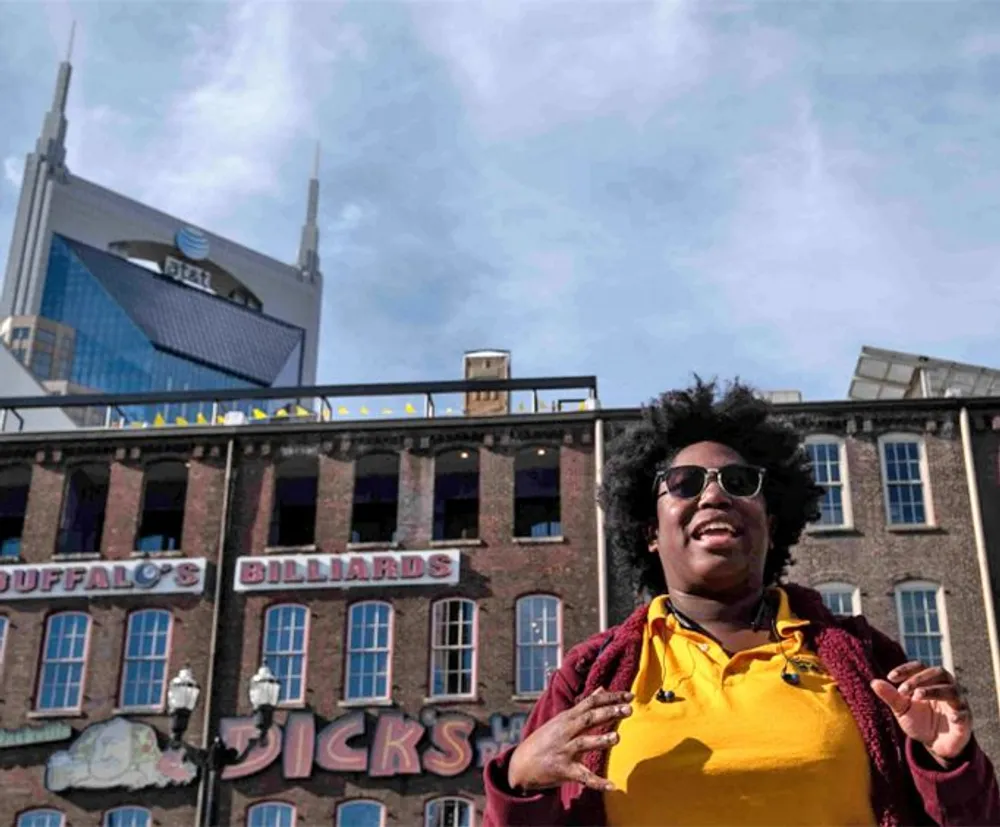 A person in a yellow shirt and sunglasses is pictured in the foreground with historic-looking buildings and a modern skyscraper in the background