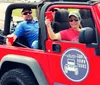 Two people are smiling and enjoying a ride in a red Jeep with a Top Down Tours Nashville decal on the side suggesting a leisurely tour experience