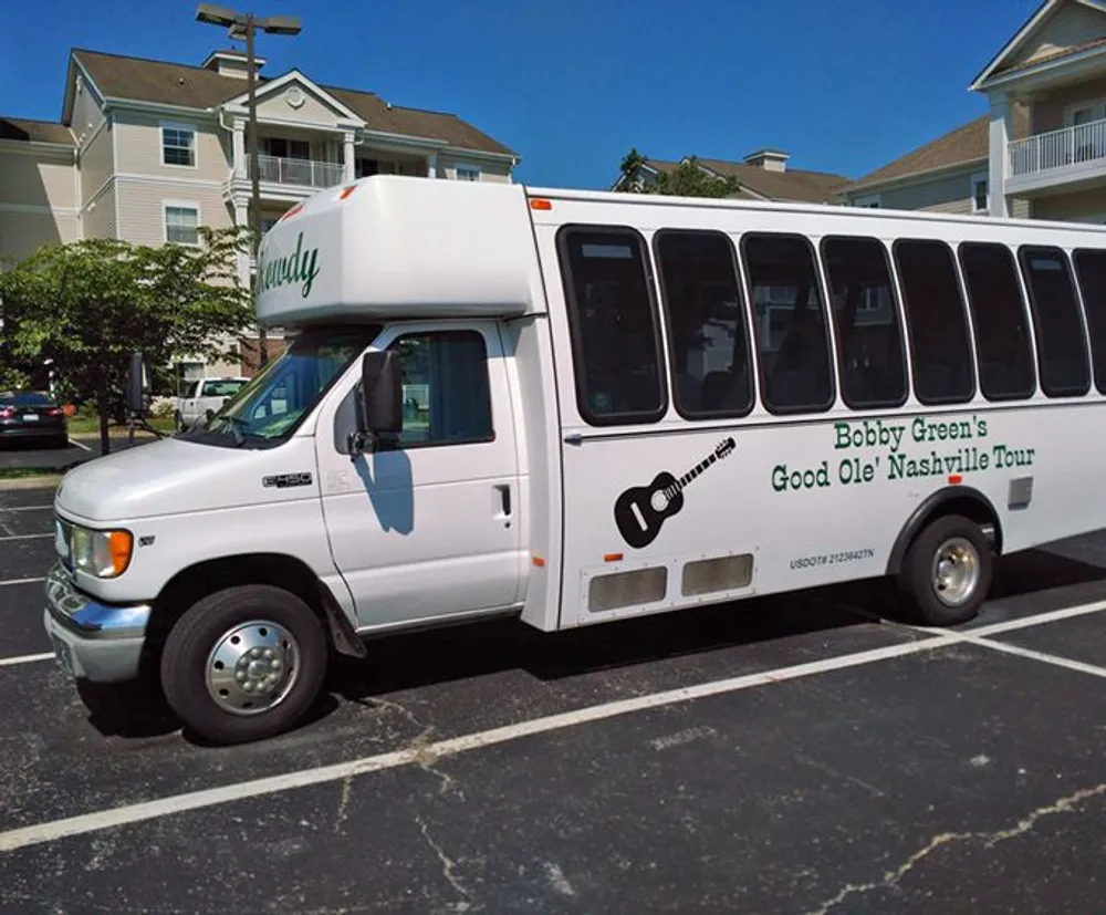 This is an image of a white passenger shuttle bus labeled Bobby Greens Good Ole Nashville Tour parked in a lot with buildings in the background