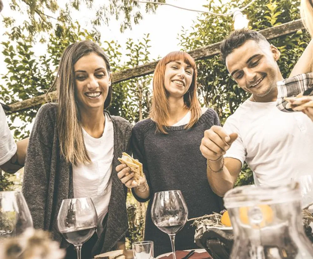 A group of people is sharing a joyful moment around a table with empty wine glasses suggesting they are at a social gathering or celebration