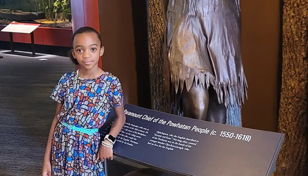 A young girl stands next to an educational exhibit about the Paramount Chief of the Powhatan People