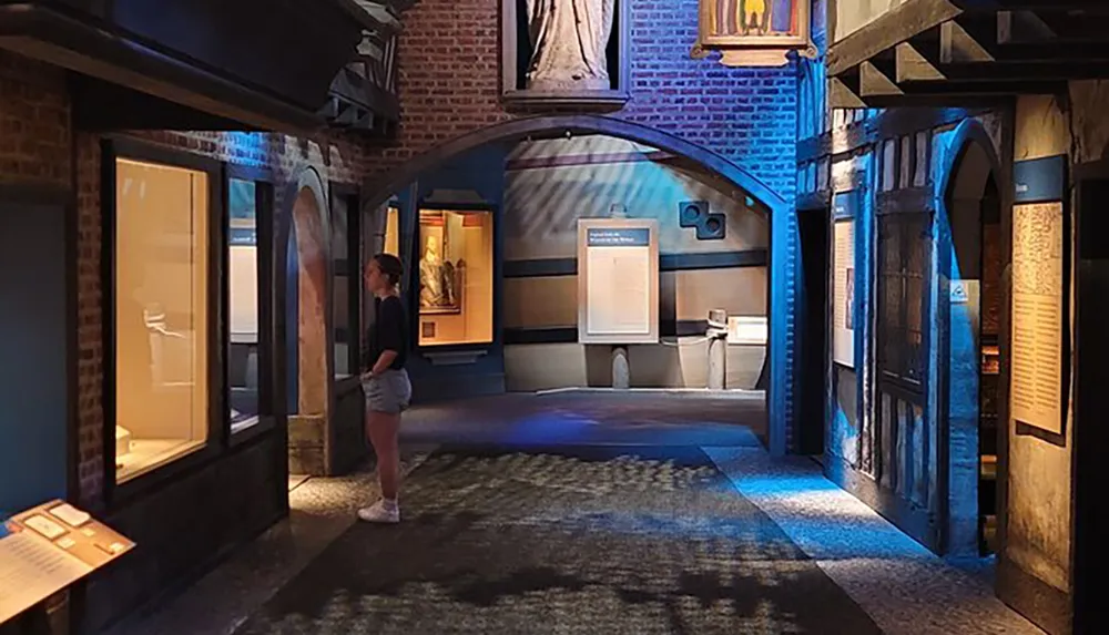 A person is observing exhibits in a dimly lit museum gallery designed to mimic a historical street scene