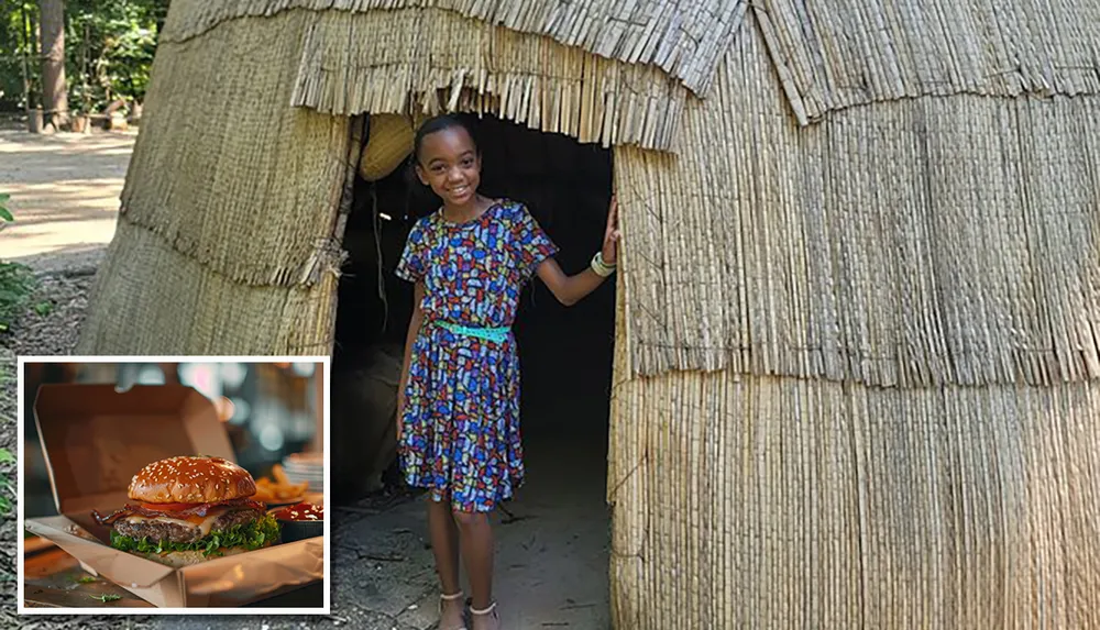 A smiling child is standing in the doorway of a thatch-roofed hut
