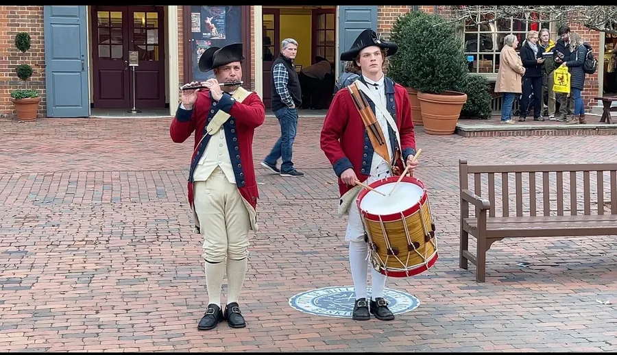 Two individuals dressed in historical uniforms play the flute and drum in what appears to be a reenactment or historical presentation.